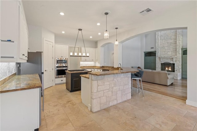 kitchen featuring kitchen peninsula, stainless steel appliances, white cabinetry, hanging light fixtures, and a breakfast bar area