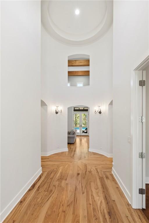 corridor with light wood-type flooring, a tray ceiling, and french doors