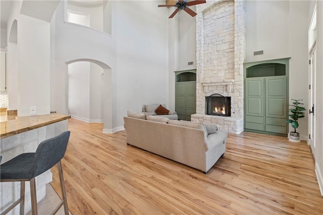 living room featuring ceiling fan, a stone fireplace, light wood-type flooring, and a high ceiling