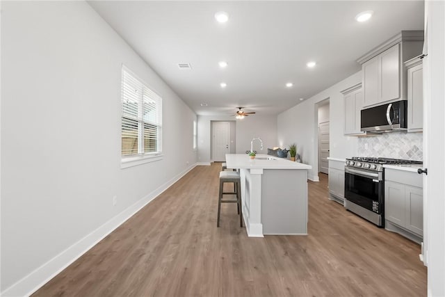 kitchen featuring a center island with sink, gray cabinets, stainless steel appliances, and a breakfast bar area