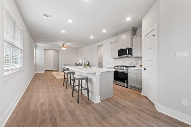 kitchen with a breakfast bar, decorative backsplash, gray cabinets, an island with sink, and stainless steel appliances