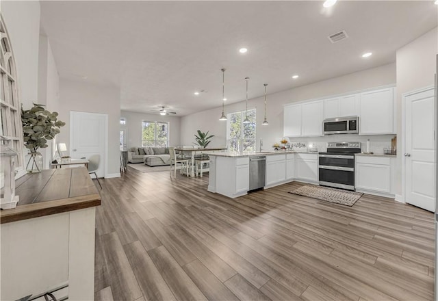 kitchen featuring pendant lighting, white cabinets, light hardwood / wood-style flooring, kitchen peninsula, and stainless steel appliances