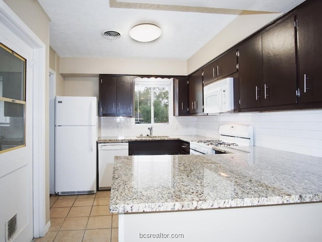 kitchen featuring kitchen peninsula, backsplash, light stone counters, dark brown cabinets, and white appliances