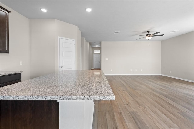 kitchen with a center island, a ceiling fan, dark brown cabinets, light wood-type flooring, and baseboards