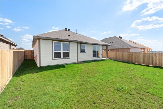 rear view of house with a fenced backyard, a shingled roof, and a lawn