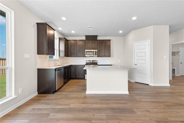 kitchen with dark brown cabinets, appliances with stainless steel finishes, a kitchen island, and light wood-style floors