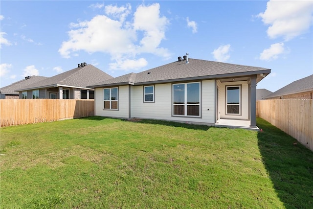 rear view of property featuring a shingled roof, a fenced backyard, and a yard