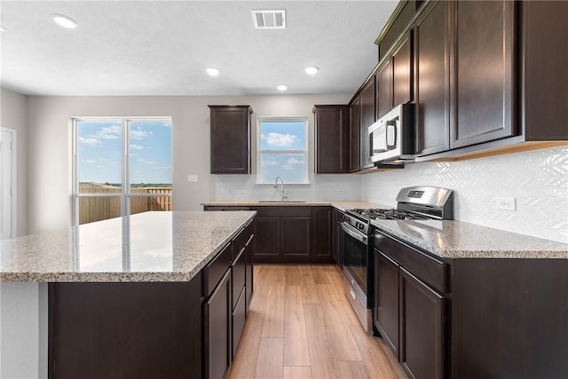 kitchen with dark brown cabinetry, a center island, stainless steel appliances, light wood-style floors, and a sink