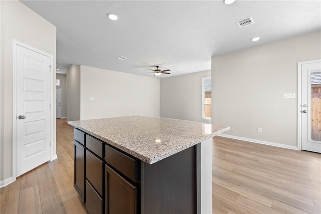 kitchen featuring a center island, light wood-style floors, a ceiling fan, light stone countertops, and baseboards