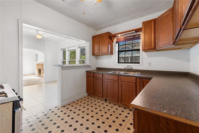 kitchen with a brick fireplace, ceiling fan, stove, and sink