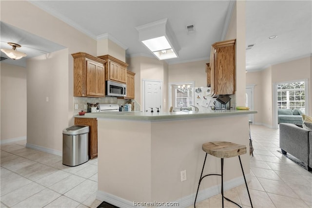 kitchen with kitchen peninsula, decorative backsplash, light tile patterned floors, and ornamental molding