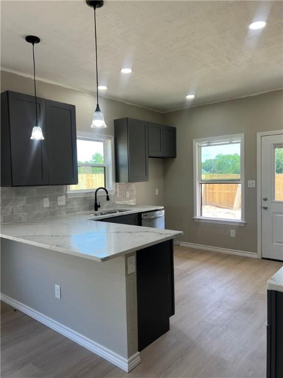 kitchen with backsplash, sink, decorative light fixtures, light stone counters, and kitchen peninsula