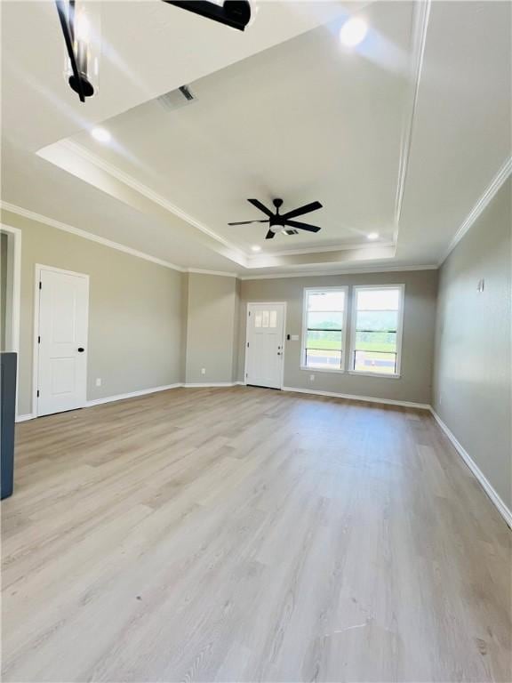 empty room with light wood-type flooring, a tray ceiling, ceiling fan, and crown molding