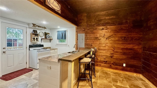 kitchen featuring wood walls, a kitchen breakfast bar, sink, white range with electric stovetop, and white cabinetry