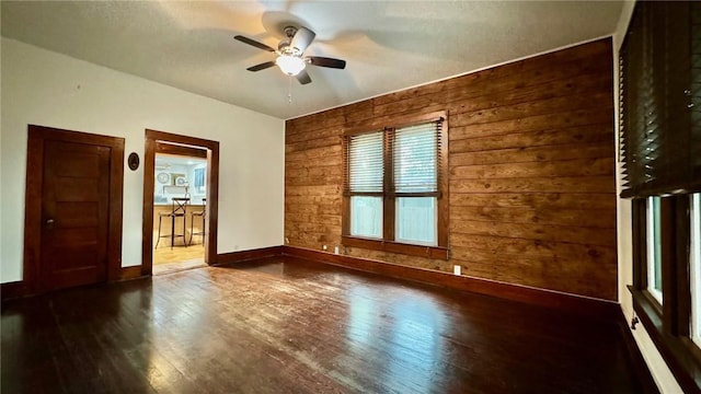 empty room with wooden walls, ceiling fan, and dark wood-type flooring