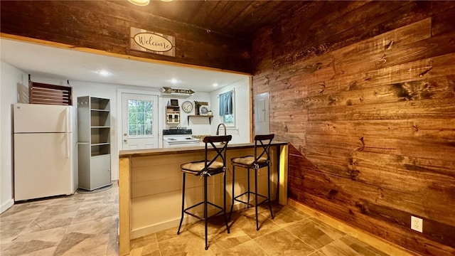 kitchen featuring sink, white appliances, a kitchen bar, wooden walls, and wood ceiling