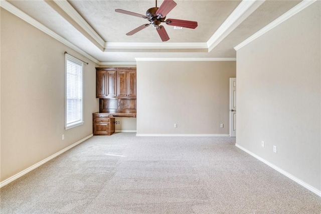 unfurnished room with a raised ceiling, a ceiling fan, crown molding, baseboards, and built in study area