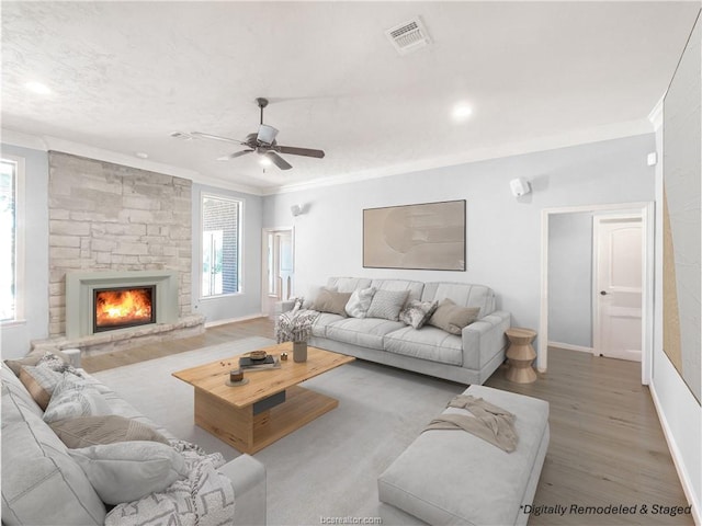 living room featuring a stone fireplace, crown molding, ceiling fan, and wood-type flooring