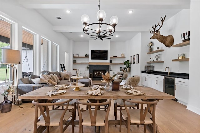 dining area featuring an inviting chandelier, sink, light hardwood / wood-style flooring, beam ceiling, and beverage cooler