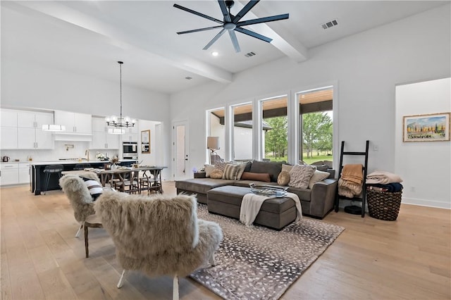 living room featuring beam ceiling, a high ceiling, light hardwood / wood-style floors, and ceiling fan with notable chandelier