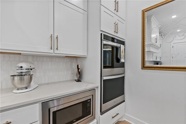 kitchen featuring white cabinets, light stone counters, appliances with stainless steel finishes, and tasteful backsplash