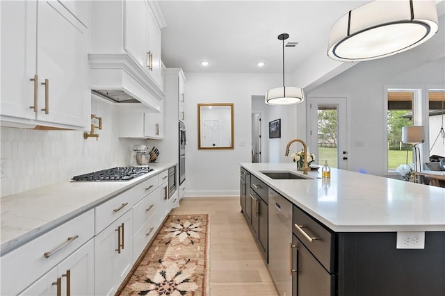 kitchen with a center island with sink, white cabinets, sink, hanging light fixtures, and tasteful backsplash