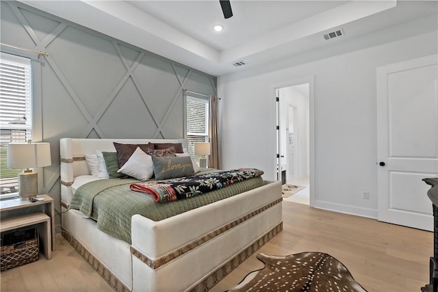 bedroom featuring light wood-type flooring, a tray ceiling, and ceiling fan