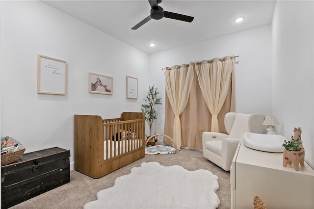 carpeted bedroom featuring ceiling fan and a crib