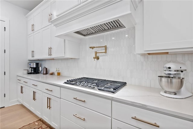 kitchen featuring stainless steel gas stovetop, premium range hood, white cabinets, light wood-type flooring, and light stone counters