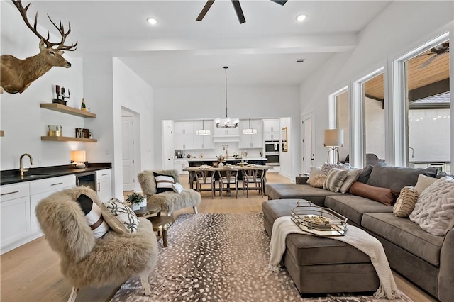 living room featuring ceiling fan with notable chandelier, sink, beam ceiling, light hardwood / wood-style floors, and wine cooler