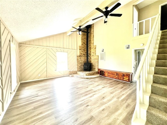 unfurnished living room featuring ceiling fan, wood-type flooring, a wood stove, and a textured ceiling