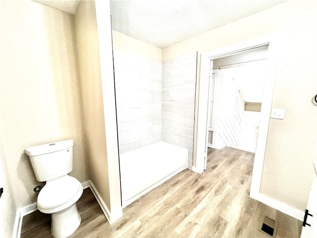 bathroom with tiled shower, hardwood / wood-style floors, a textured ceiling, and toilet