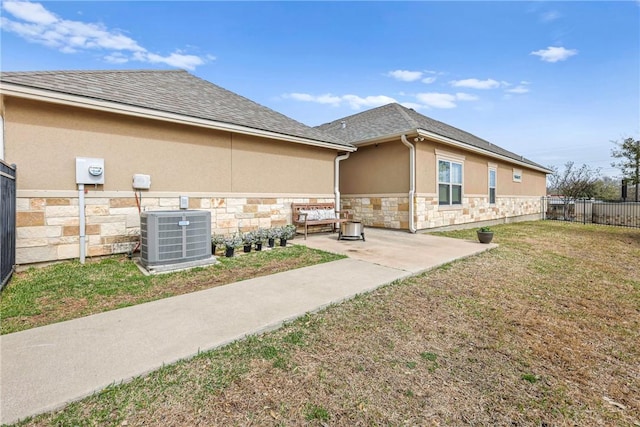 view of home's exterior featuring stone siding, fence, a yard, central AC, and stucco siding