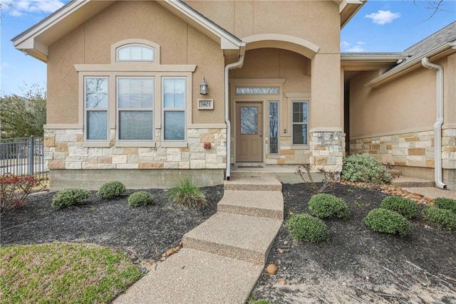 view of exterior entry featuring stone siding, fence, and stucco siding