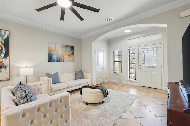 living room with arched walkways, light tile patterned floors, visible vents, a ceiling fan, and ornamental molding