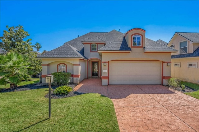 french country inspired facade featuring a shingled roof, a front lawn, stucco siding, decorative driveway, and an attached garage