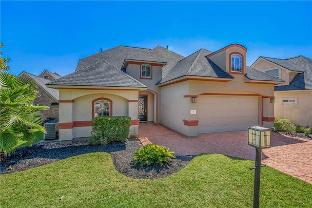 view of front facade with a shingled roof, a front lawn, stucco siding, decorative driveway, and an attached garage