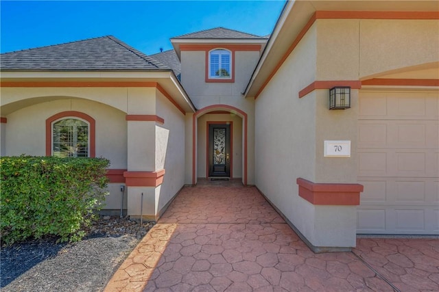 entrance to property with an attached garage, roof with shingles, and stucco siding