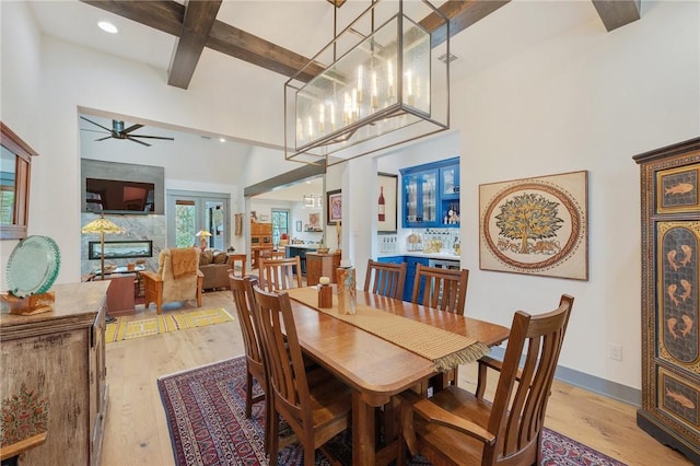 dining area featuring a high ceiling, ceiling fan, light hardwood / wood-style floors, and beam ceiling