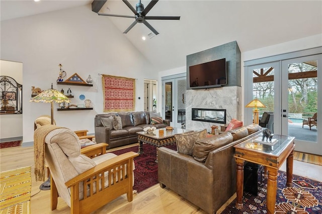 living room with french doors, high vaulted ceiling, a premium fireplace, ceiling fan, and light wood-type flooring