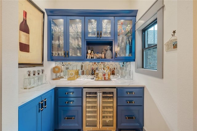 bar featuring blue cabinetry, light stone countertops, beverage cooler, and tasteful backsplash