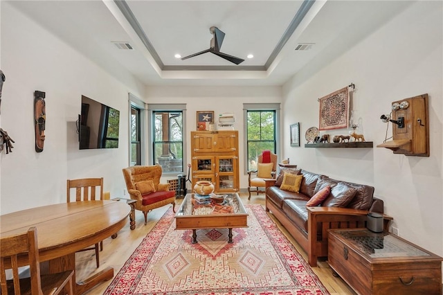 living room featuring light wood-type flooring, a tray ceiling, and ceiling fan