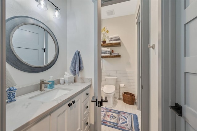 bathroom featuring toilet, tile walls, and vanity