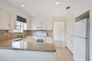 kitchen featuring kitchen peninsula, backsplash, white appliances, white cabinets, and light stone counters