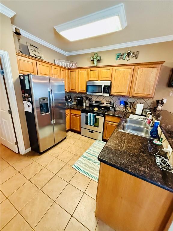 kitchen featuring backsplash, crown molding, a sink, light tile patterned floors, and stainless steel appliances