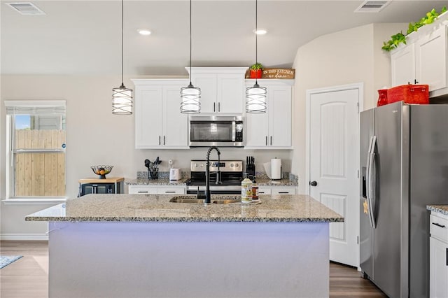 2110 Chief St, Bryan, TX 77807 - kitchen with appliances with stainless steel finishes, a sink, wood finished floors, white cabinetry, and a kitchen island with sink