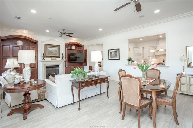 living room with ceiling fan, crown molding, a fireplace, and light hardwood / wood-style flooring