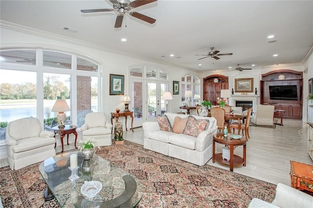 living room with ceiling fan, light wood-type flooring, crown molding, and a wealth of natural light