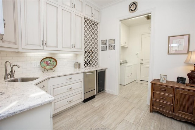 kitchen with light stone countertops, sink, white cabinetry, washing machine and clothes dryer, and wine cooler