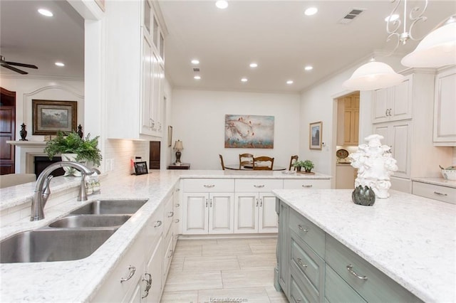 kitchen featuring white cabinets, light stone countertops, hanging light fixtures, and sink